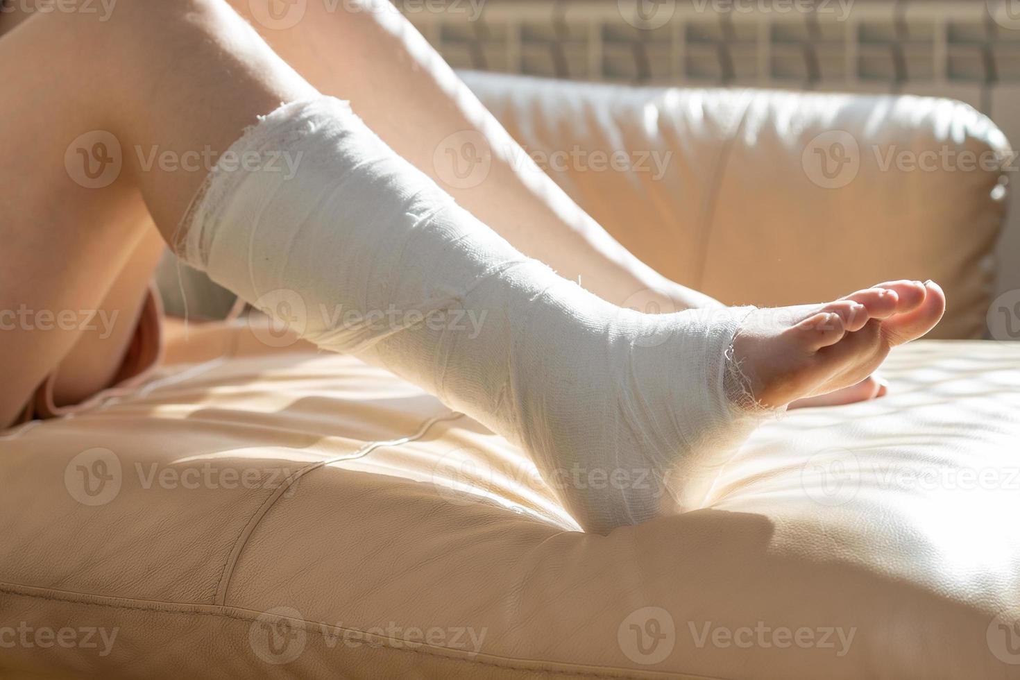Girl with a cast on their leg, sitting on the couch and drawing on a graphics tablet. Bandaged leg cast and toes after a running injury accident. Teen girl in a plaster cast. Cropped shot of a girl. photo