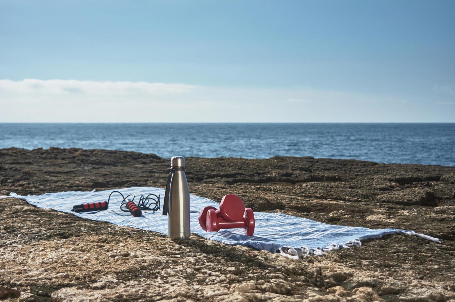 Fondo de concepto de fitness y deportes. preparándose toalla, cuerda para saltar, campana y botella de agua, junto al mar en un soleado día de invierno, con un hermoso cielo azul foto