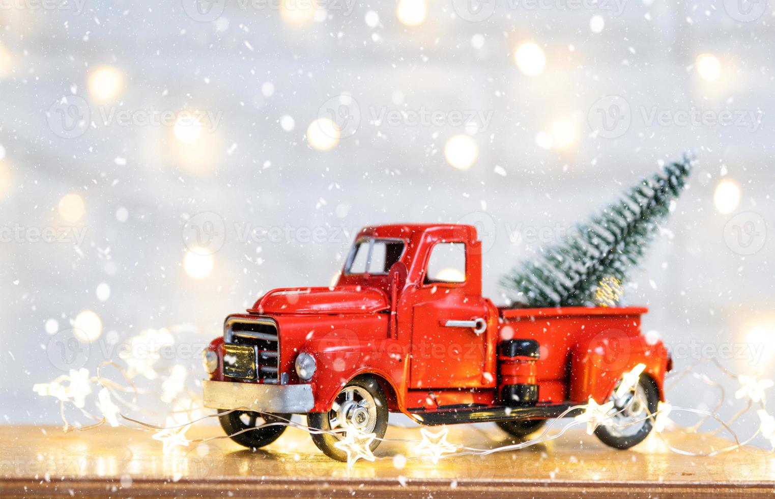decoración navideña camioneta roja retro en la nieve con luces de hadas en el árbol de navidad bokeh. tarjeta de felicitación de año nuevo. hogar acogedor foto