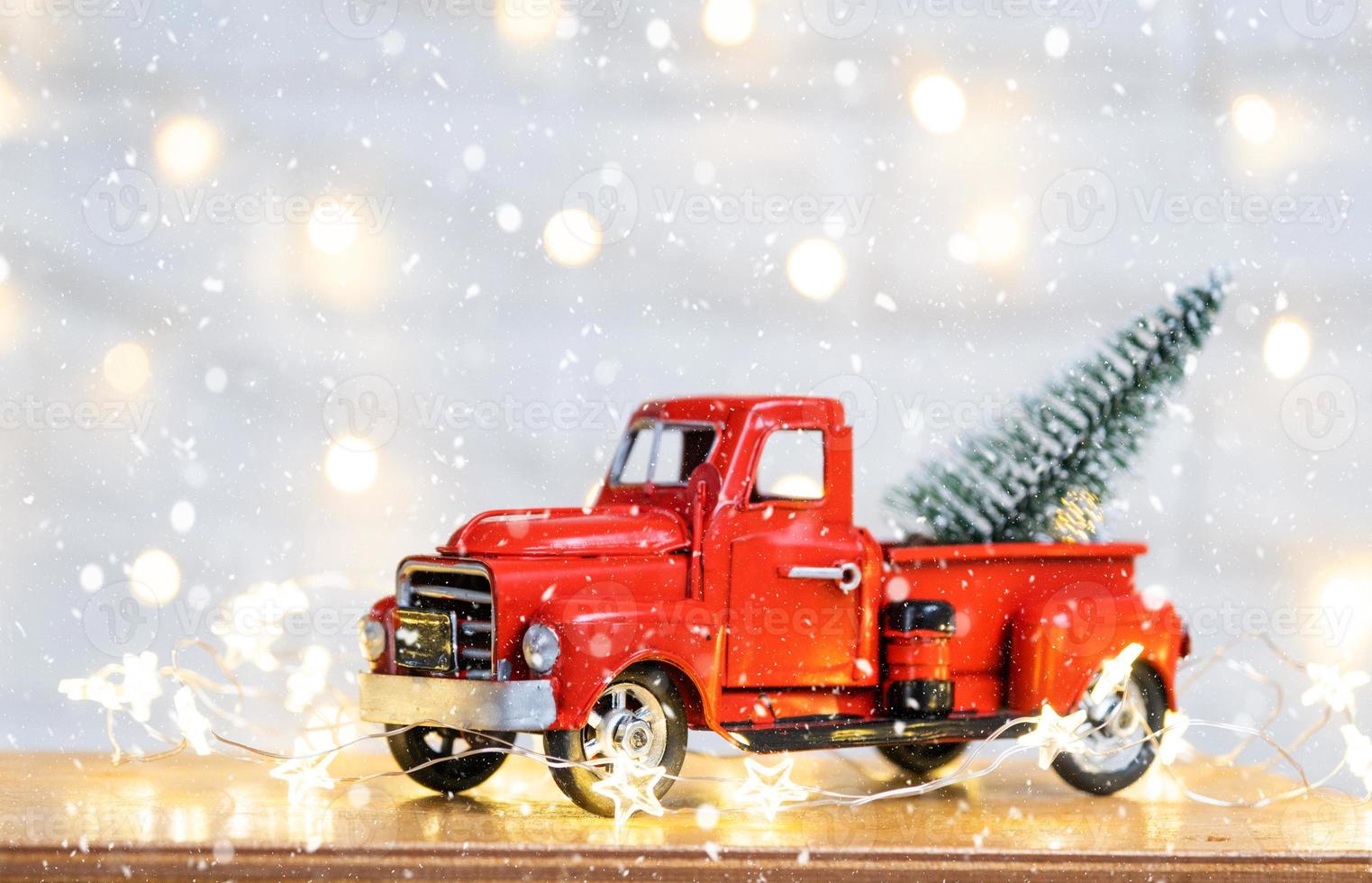 Christmas decor red retro car pickup truck on snow with fairy lights in bokeh Christmas tree. New Year greeting card. Cozy home photo