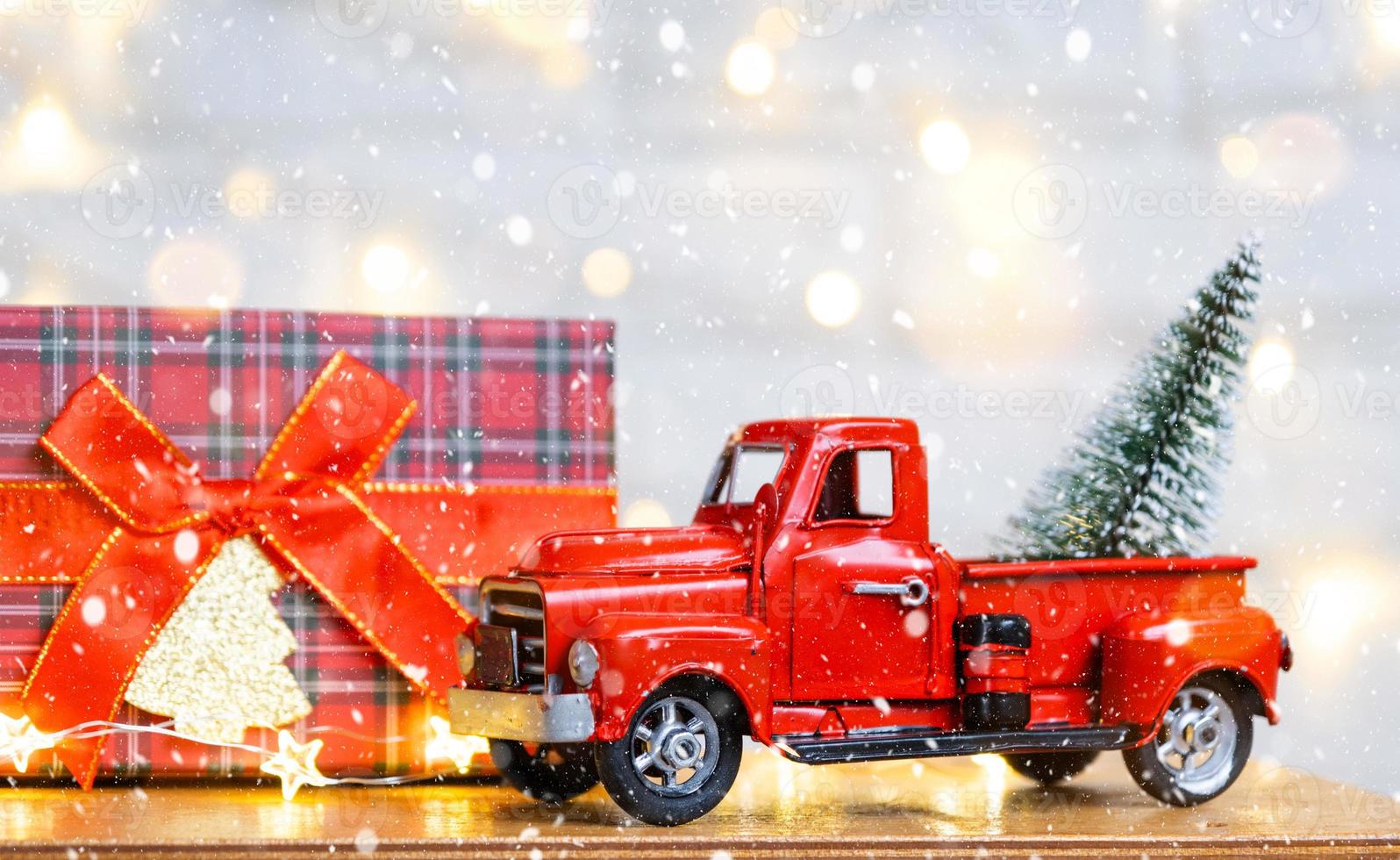 Christmas decor red retro car pickup truck on snow with fairy lights in bokeh Christmas tree. New Year greeting card. Cozy home photo