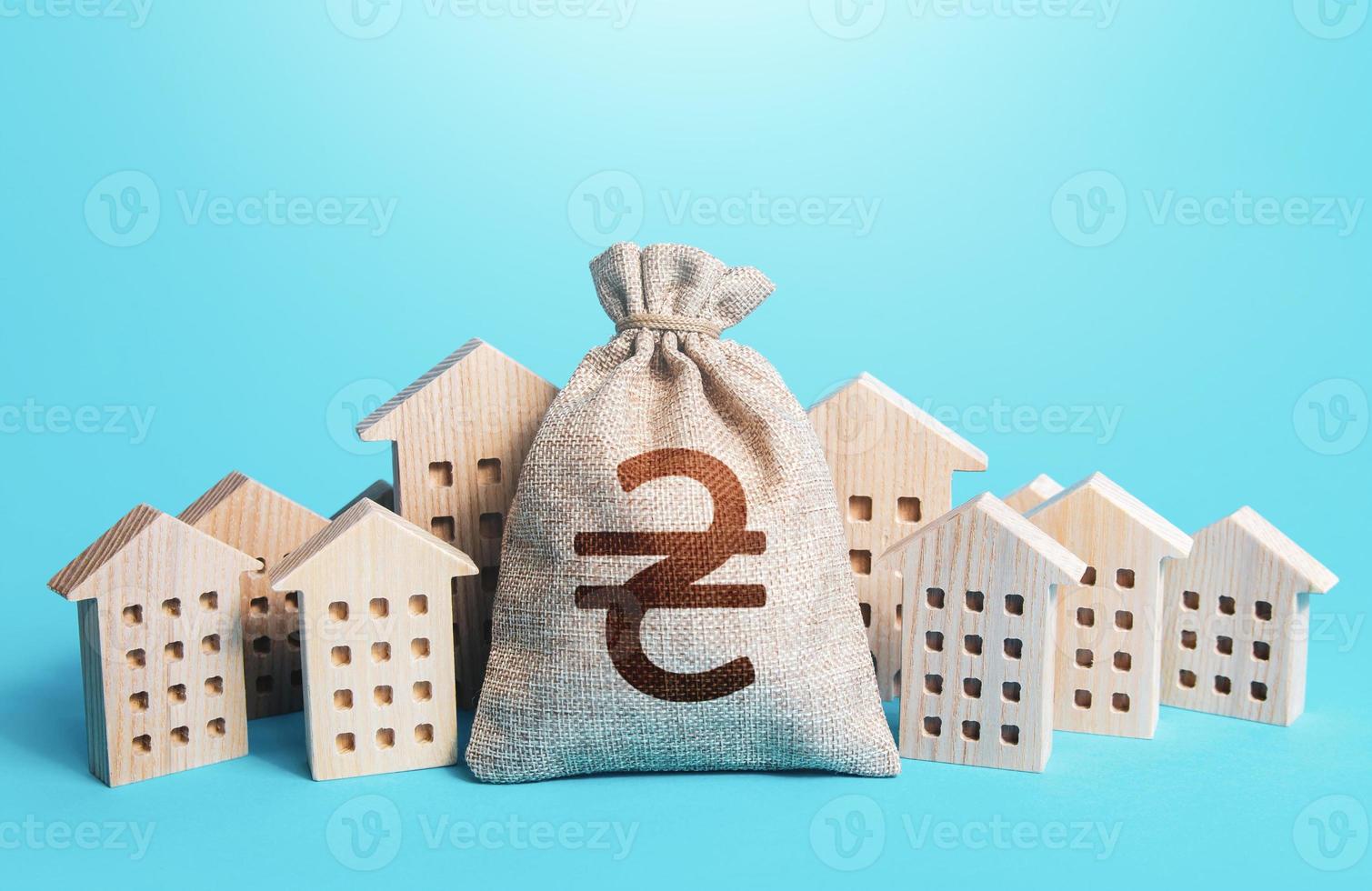 Ukrainian hryvnia money bag among town houses figurines. Municipal budgeting. Rental business. Realtor services. Sale of real estate. property taxes. Tax collection, investment in city development. photo