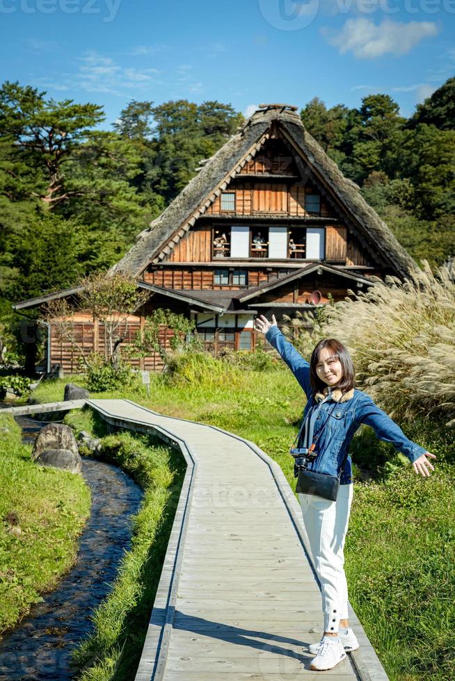 Beautiful Japanese girl with a background of Shirakawago village during autumn with a triangle house, rice field, and pine mountain. photo
