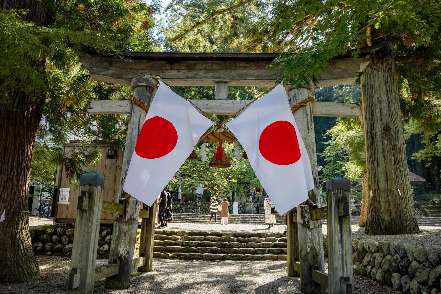 Shirakawago, Gifu, Japan - Ocotber 2022 - Shirakawa Hachiman Shrine gate area at Shirakawago village with pine trees and Japanese flag. photo