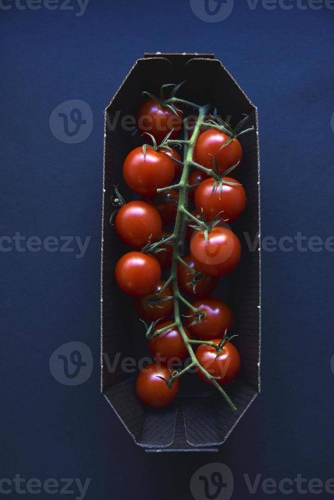 Small cherry tomatoes are yellow and red in a paper container. Small tomatoes on a black background. photo