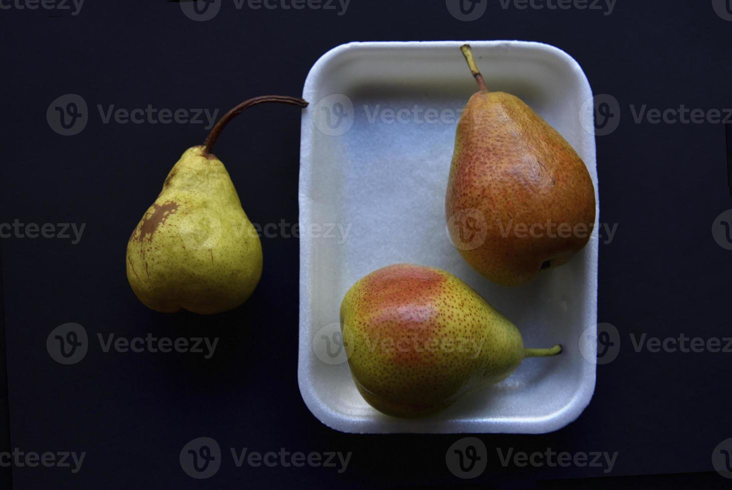 Red and green pears on a black background. Pears in a package from the store. Beautiful fruits of pears. photo