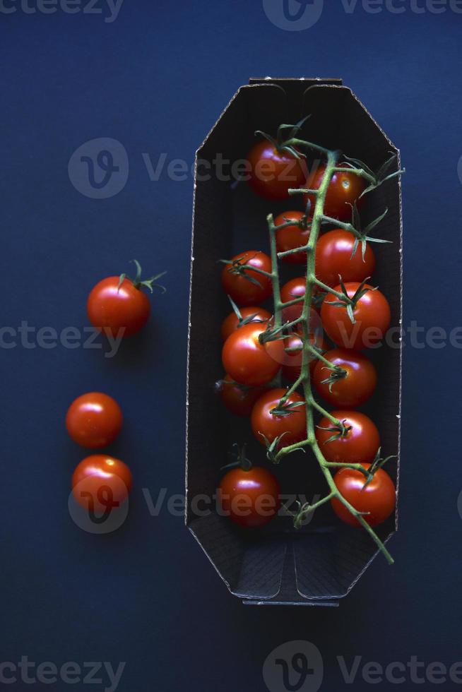 Small cherry tomatoes are yellow and red in a paper container. Small tomatoes on a black background. photo