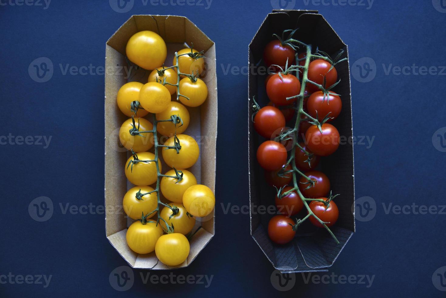 Small cherry tomatoes are yellow and red in a paper container. Small tomatoes on a black background. photo