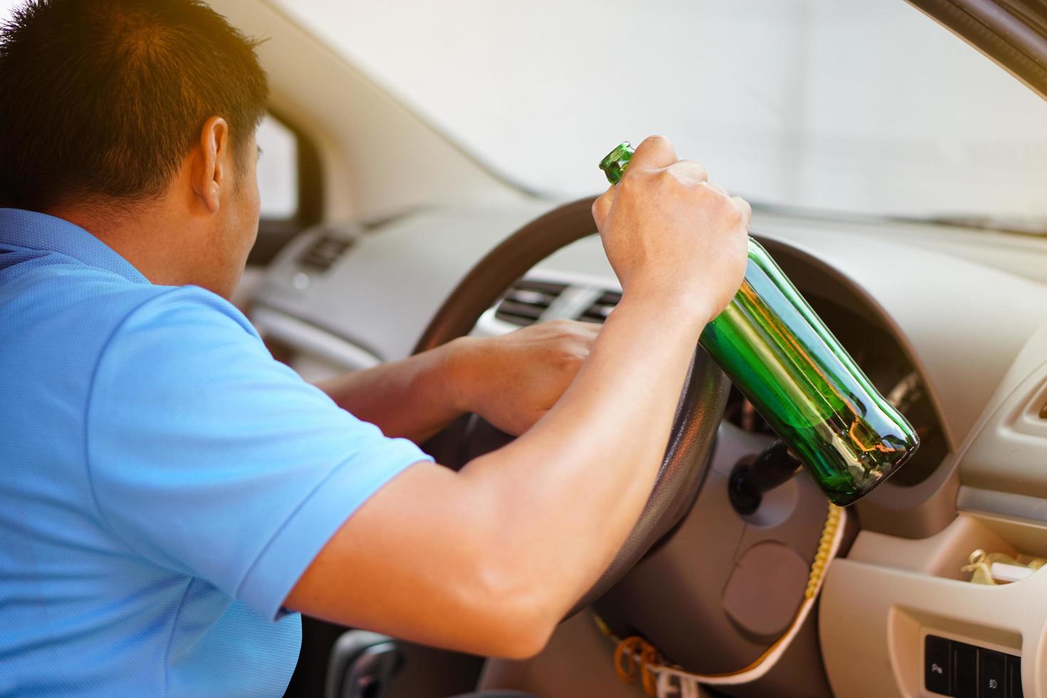 un borracho asiático sostiene una botella de cerveza para beber en el auto. concepto, deja de conducir mientras bebes alcohol o campaña de whisky. ilegal y peligroso conducir un vehículo que conduce a un accidente. foto