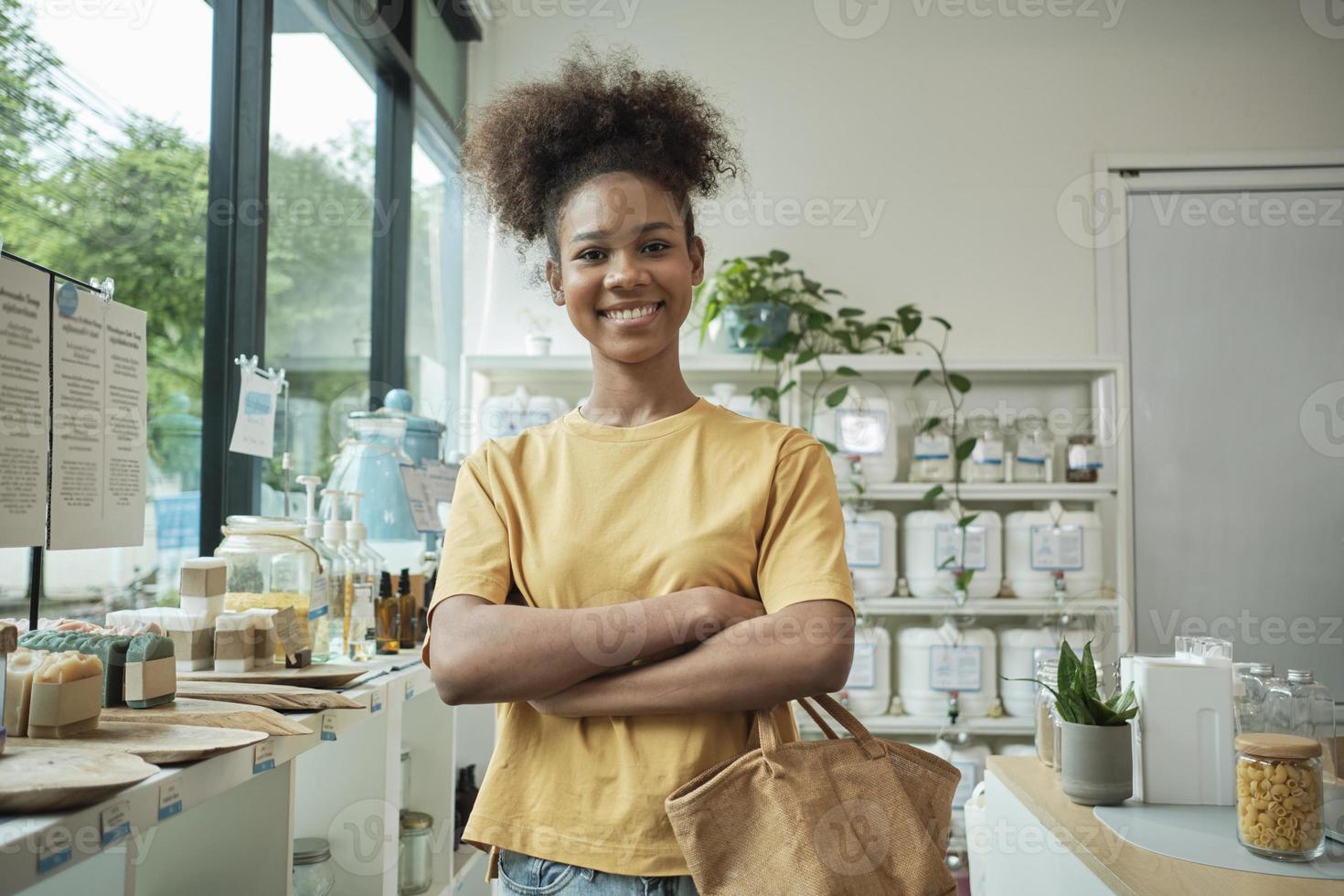 Portrait of young African American female customer with a reusable shopping bag happy smiles in refill store, zero-waste retail grocery, and plastic-free, environment-friendly, sustainable lifestyle. photo