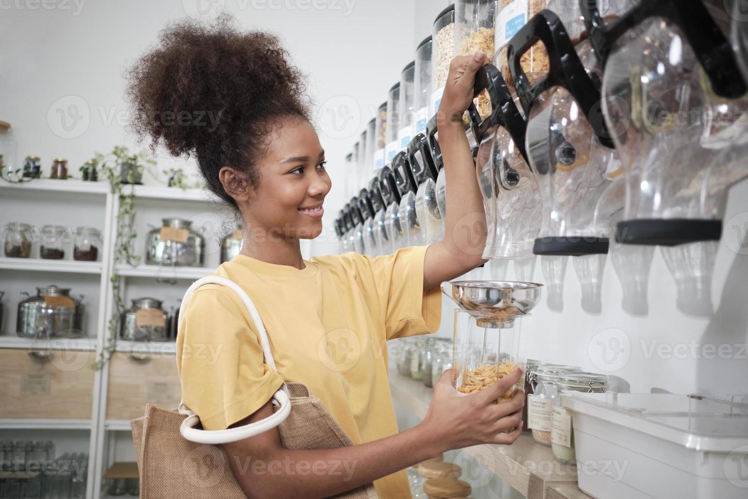 African American female customer fills cereal foods in glass jar, lever the reusable container in a refill store, and zero-waste and plastic-free grocery, environment-friendly, sustainable lifestyles. photo