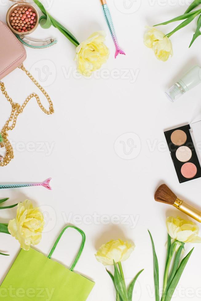 marco plano de escritorio de mesa de vista superior. espacio de trabajo de escritorio de blogger femenino con cosméticos, lápiz labial y flores de tulipán sobre fondo blanco. foto