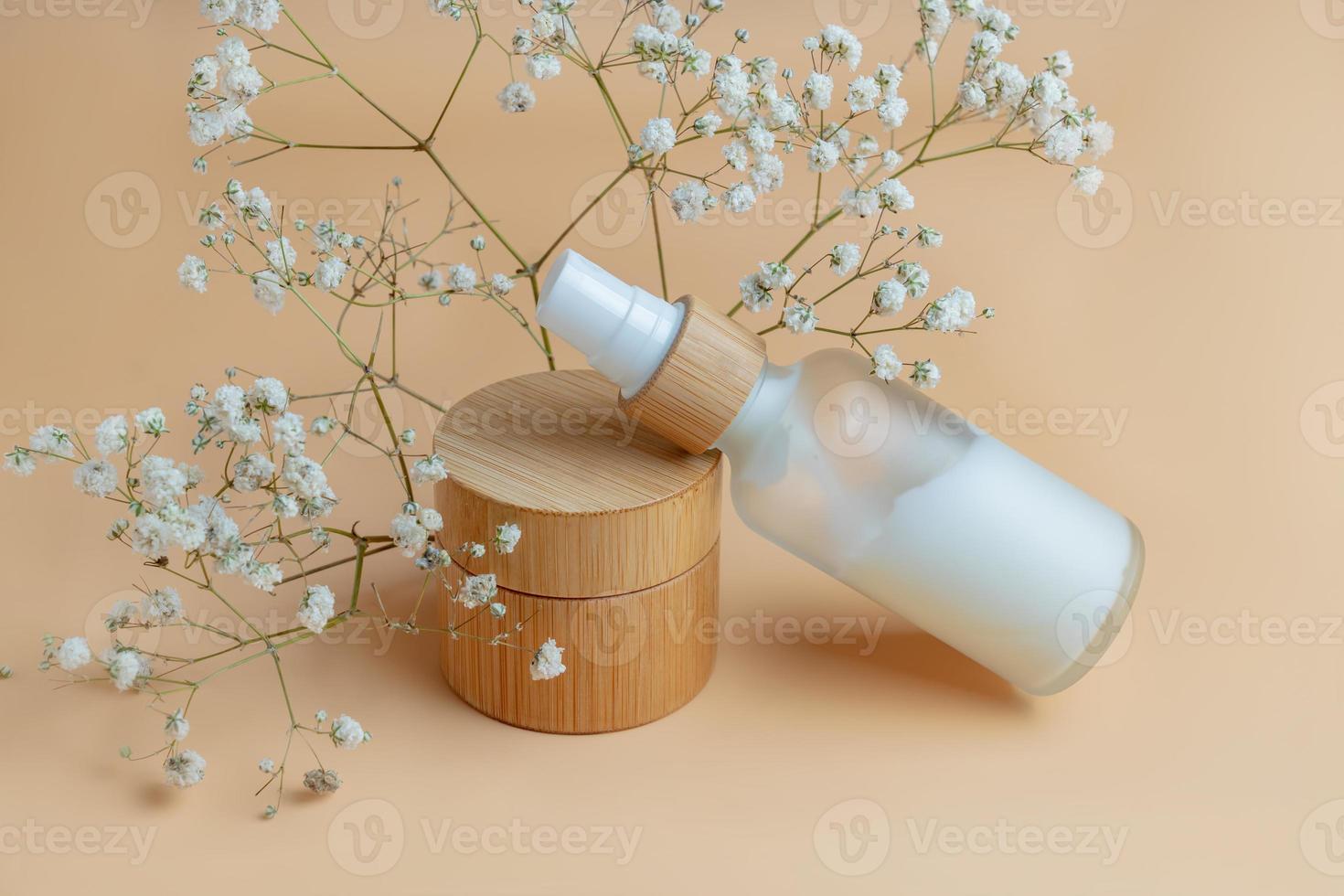 Pomp bottle with face fluid and bamboo jar with cream on beige background with dry flowers. Skincare serum or essential oil natural cosmetic. Beauty concept for face and body care. Mockup photo