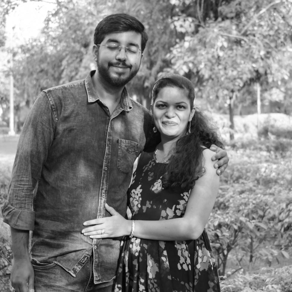 Indian couple posing for maternity baby shoot. The couple is posing in a lawn with green grass and the woman is falunting her baby bump in Lodhi Garden in New Delhi, India - Black and White photo