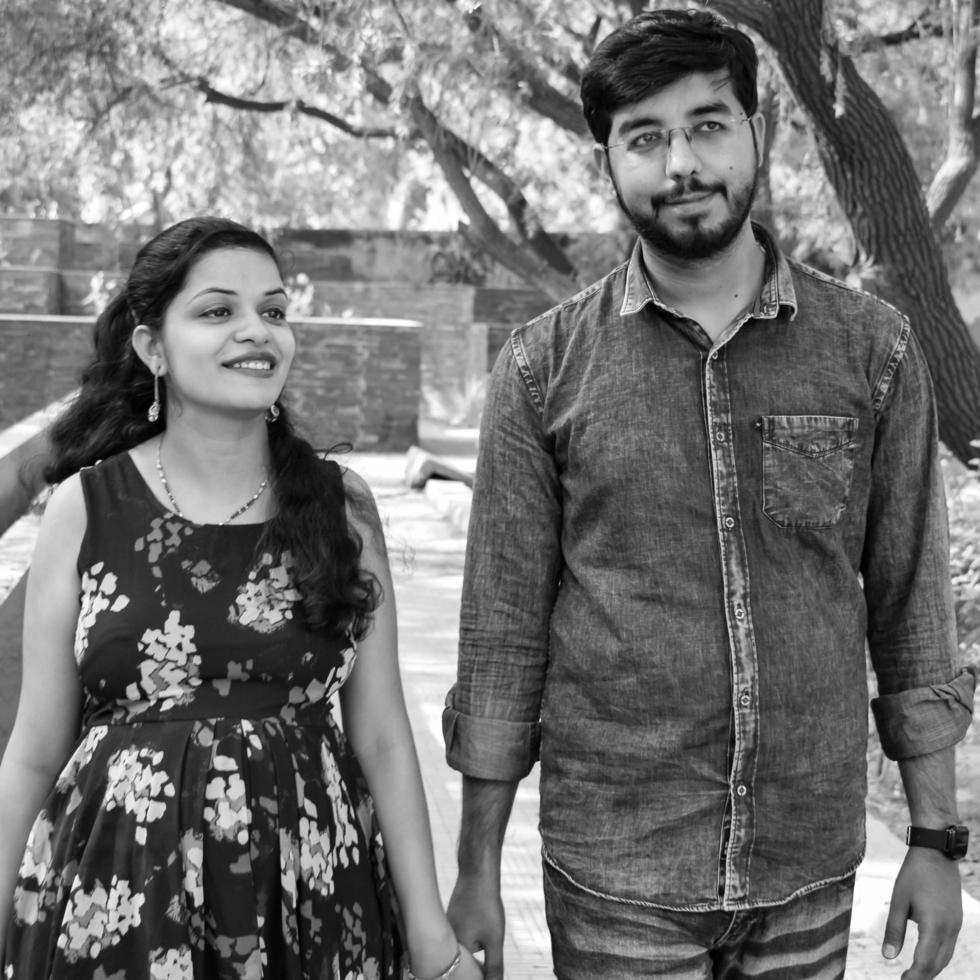 Indian couple posing for maternity baby shoot. The couple is posing in a lawn with green grass and the woman is falunting her baby bump in Lodhi Garden in New Delhi, India - Black and White photo