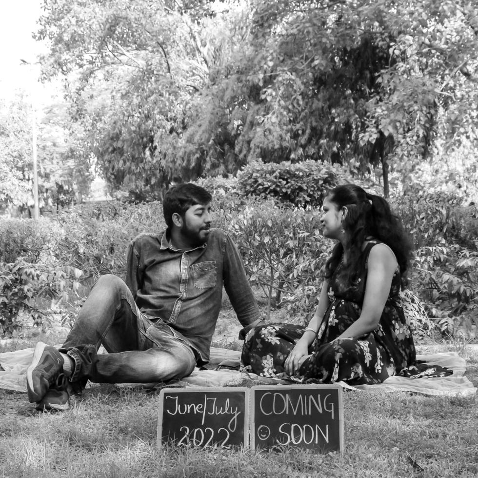 Indian couple posing for maternity baby shoot. The couple is posing in a lawn with green grass and the woman is falunting her baby bump in Lodhi Garden in New Delhi, India - Black and White photo