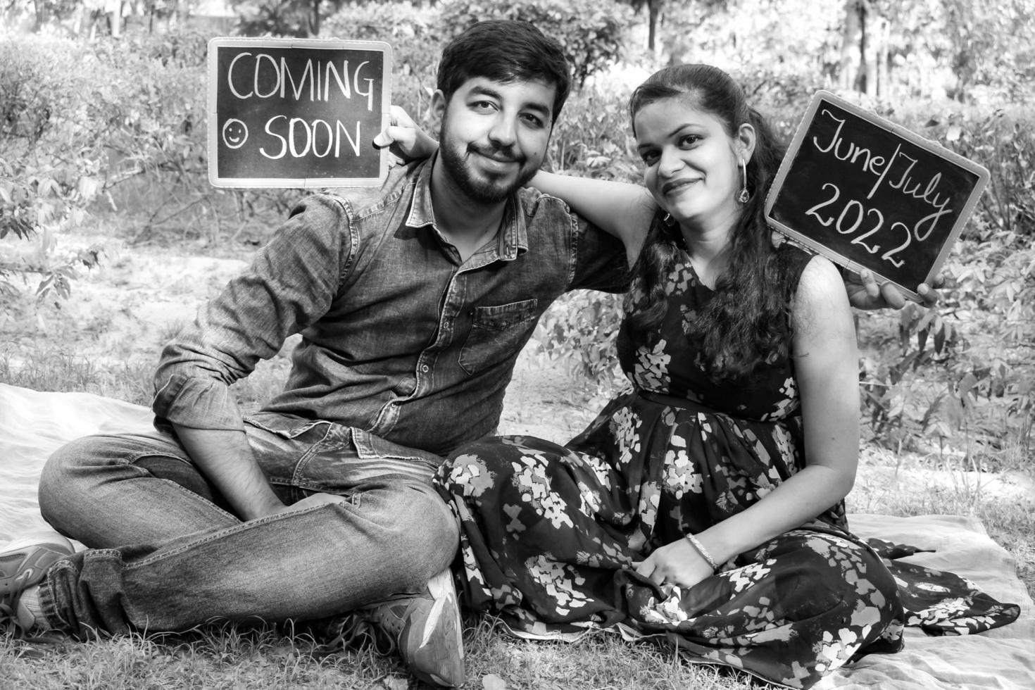 Indian couple posing for maternity baby shoot. The couple is posing in a lawn with green grass and the woman is falunting her baby bump in Lodhi Garden in New Delhi, India - Black and White photo