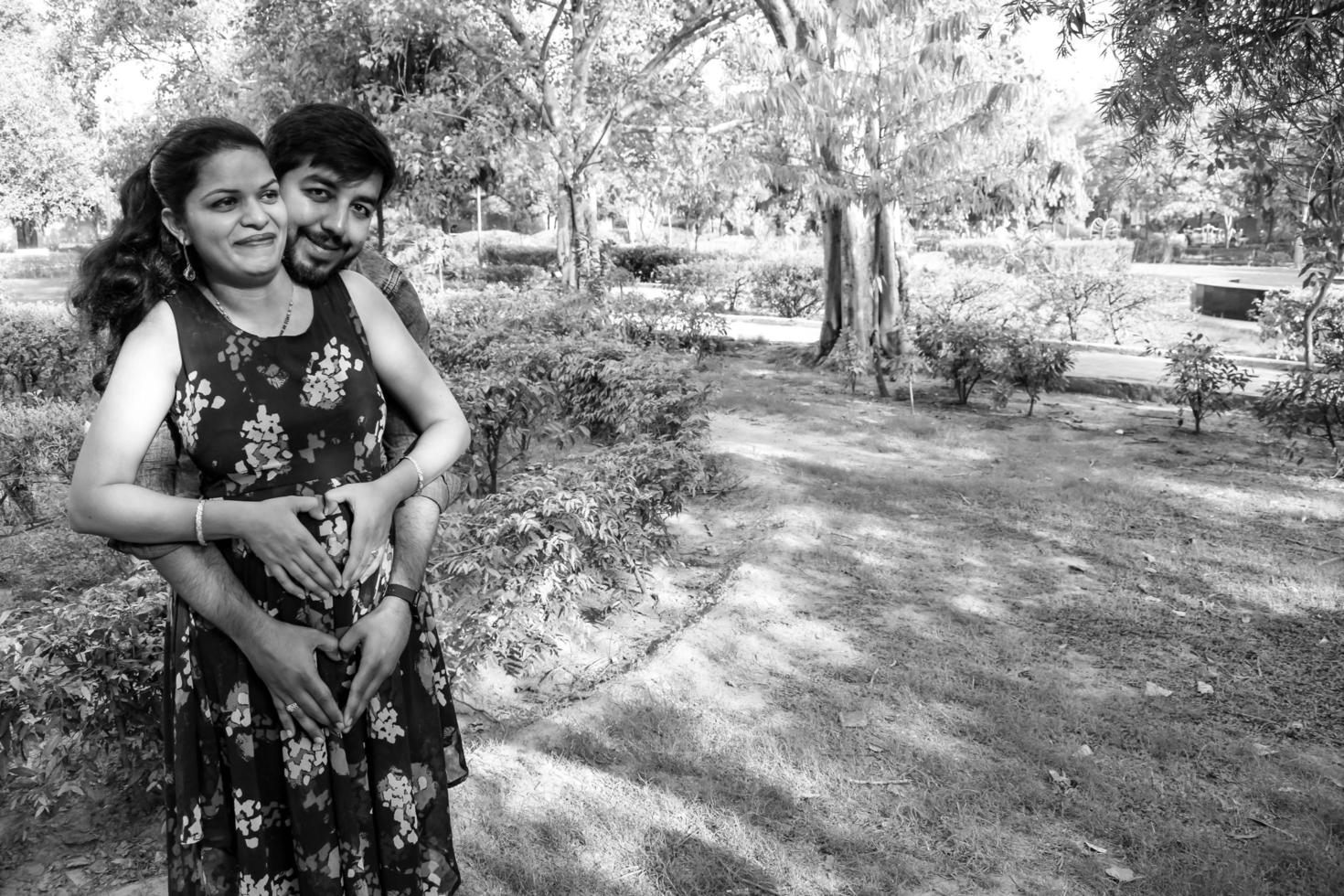 Indian couple posing for maternity baby shoot. The couple is posing in a lawn with green grass and the woman is falunting her baby bump in Lodhi Garden in New Delhi, India - Black and White photo