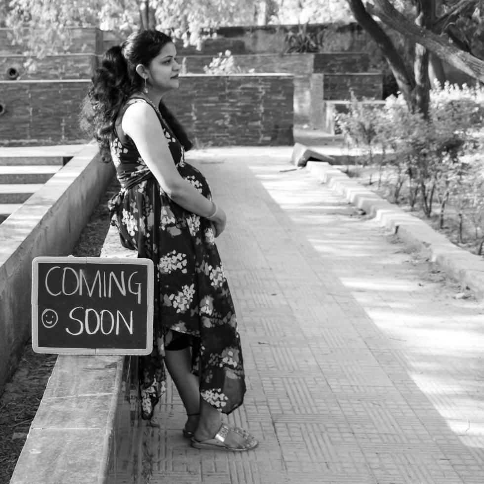 Indian couple posing for maternity baby shoot. The couple is posing in a lawn with green grass and the woman is falunting her baby bump in Lodhi Garden in New Delhi, India - Black and White photo