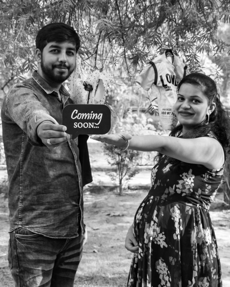 Indian couple posing for maternity baby shoot. The couple is posing in a lawn with green grass and the woman is falunting her baby bump in Lodhi Garden in New Delhi, India - Black and White photo