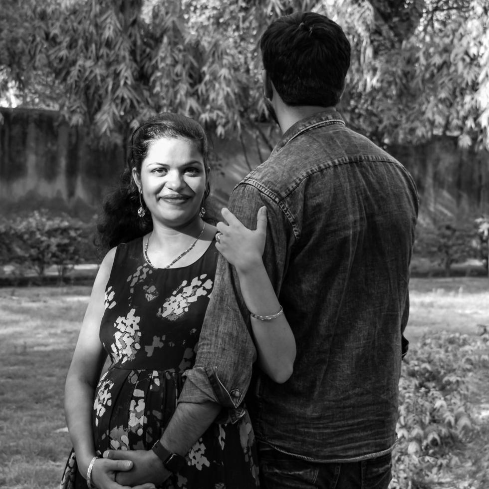 Indian couple posing for maternity baby shoot. The couple is posing in a lawn with green grass and the woman is falunting her baby bump in Lodhi Garden in New Delhi, India - Black and White photo