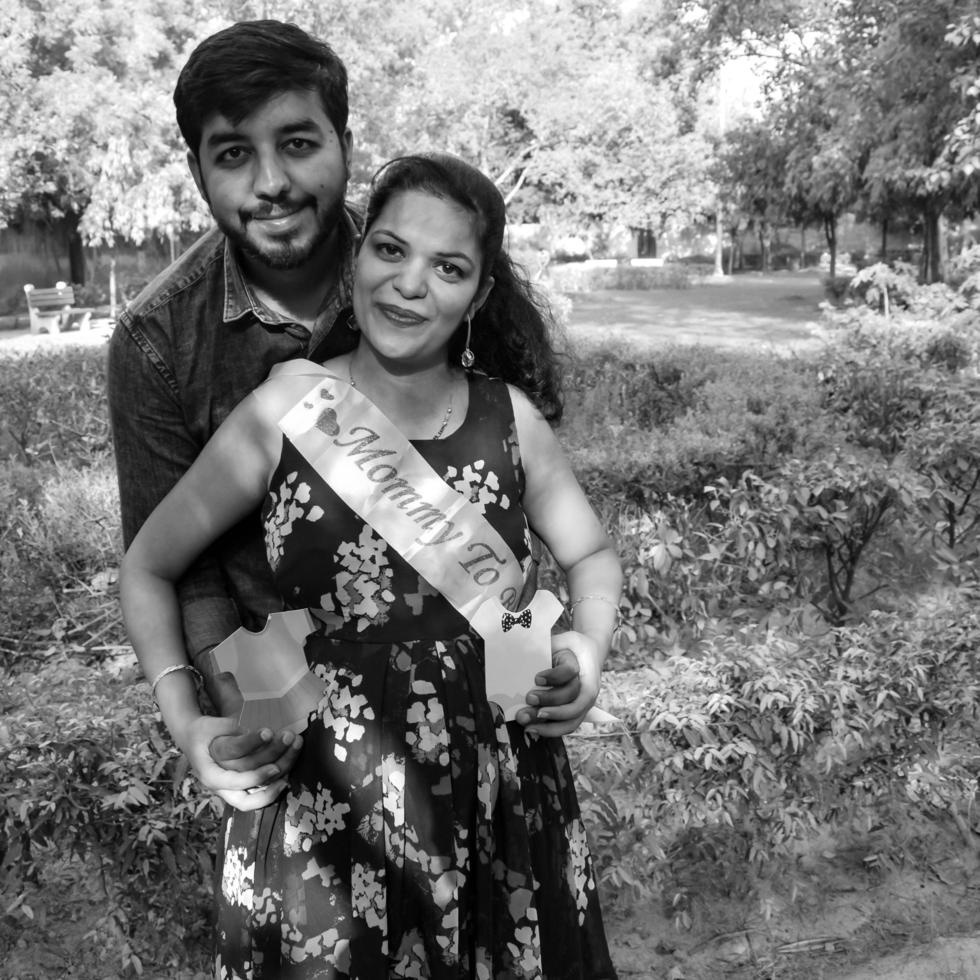 pareja india posando para una sesión de fotos de maternidad. la pareja está posando en un césped con hierba verde y la mujer está faluntando su panza en el jardín de lodhi en nueva delhi, india - blanco y negro