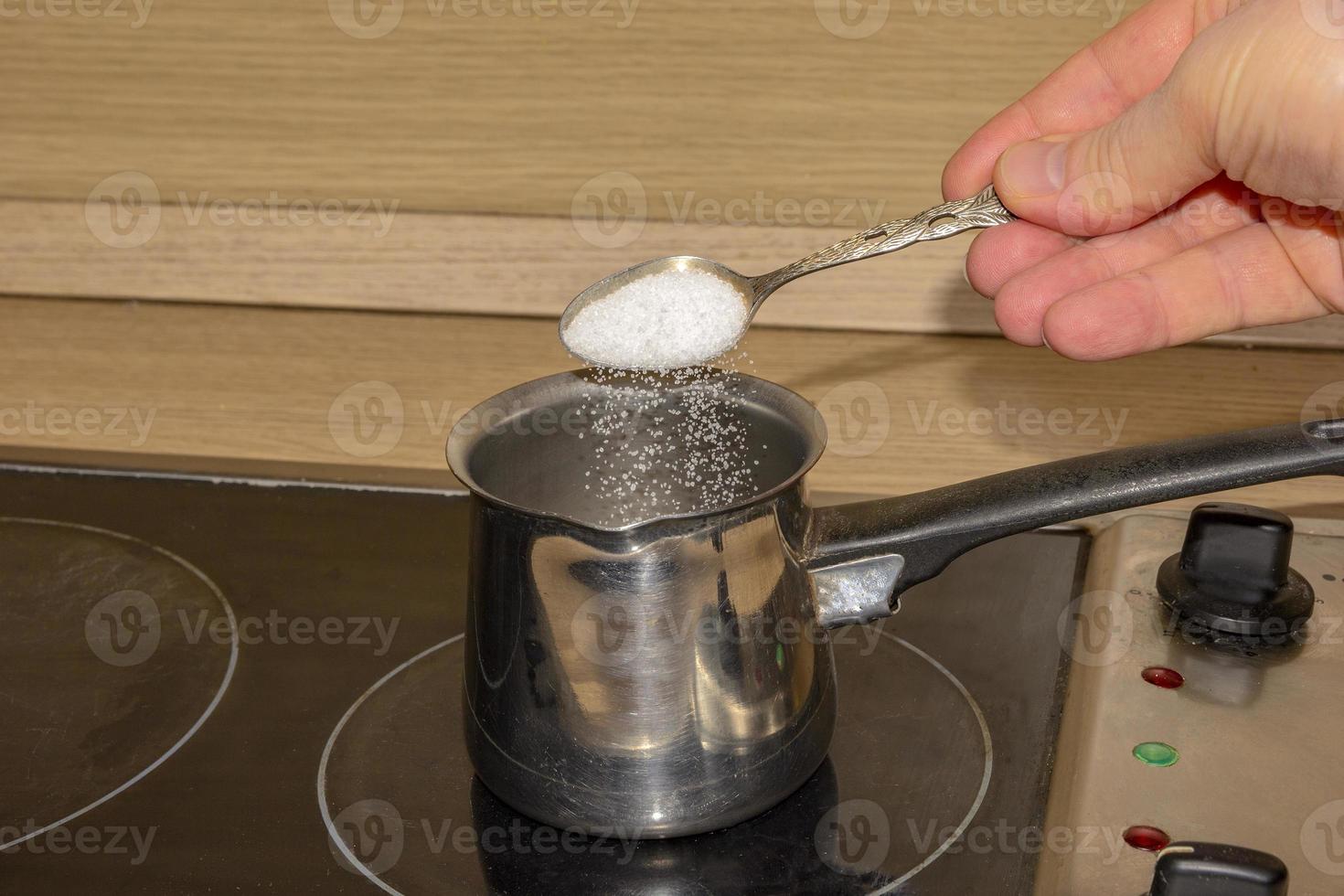 hand putting sugar with spoon in empty pot on stove photo
