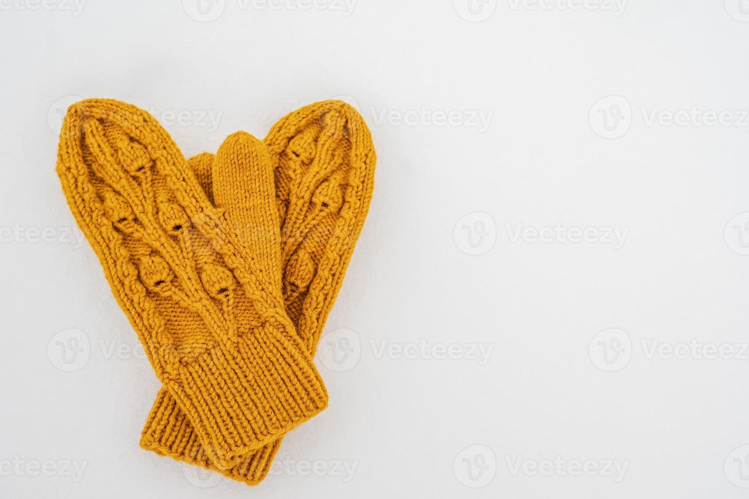 Knitted yellow mittens lie on pure white snow on a cloudy winter day. Copy space. Top view. photo