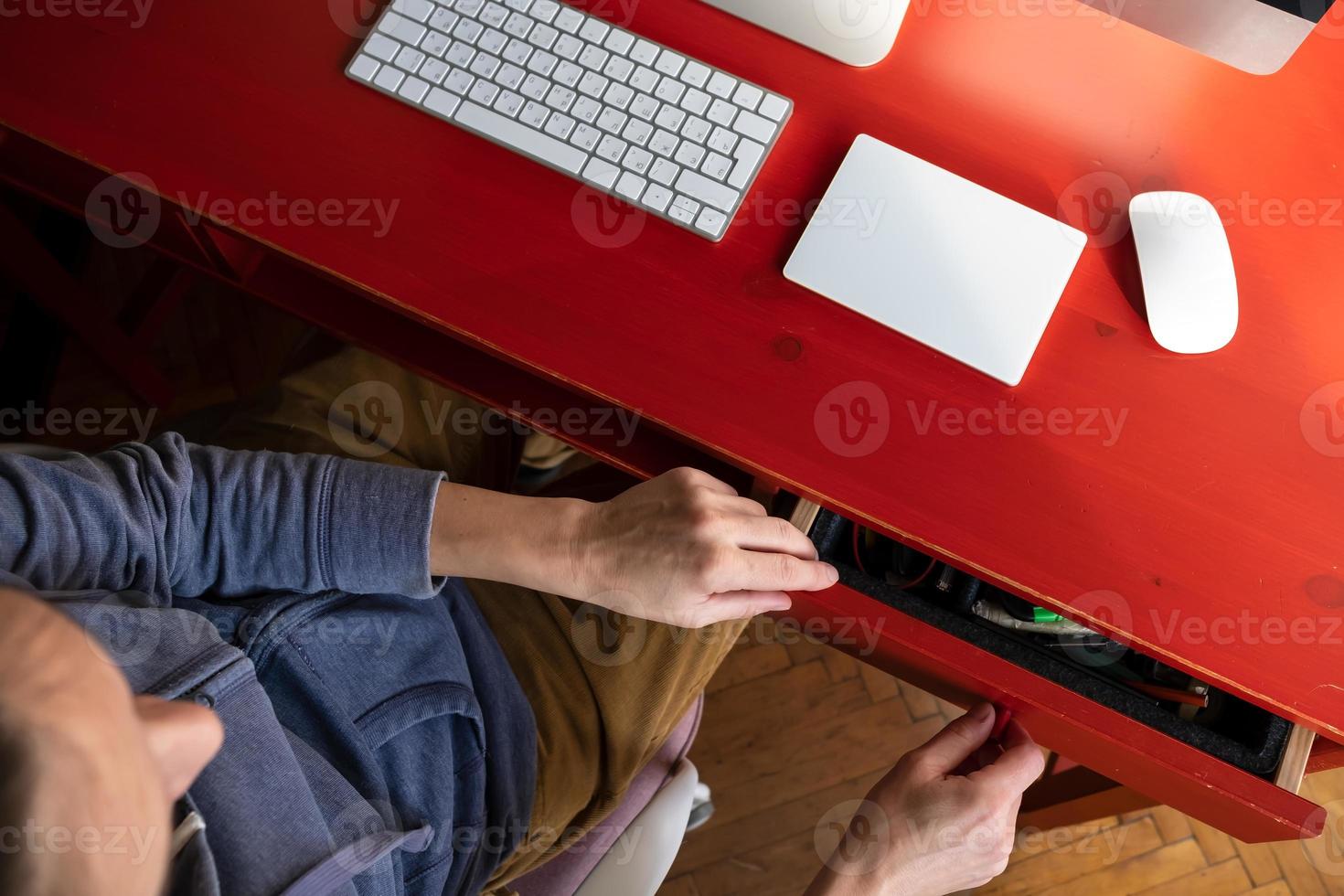 Woman opens a desktop drawer and wants to take something from there, on which there is a keyboard, touchpad and a computer. photo