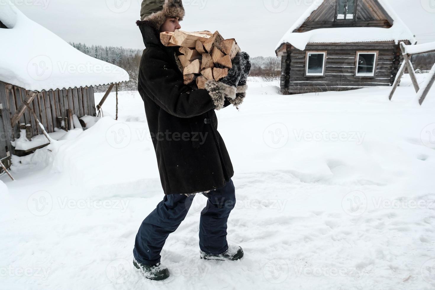 el hombre, con ropa de abrigo, lleva un puñado de leña, en un patio rural, en una noche de invierno. temporada de calefacción en el pueblo. foto