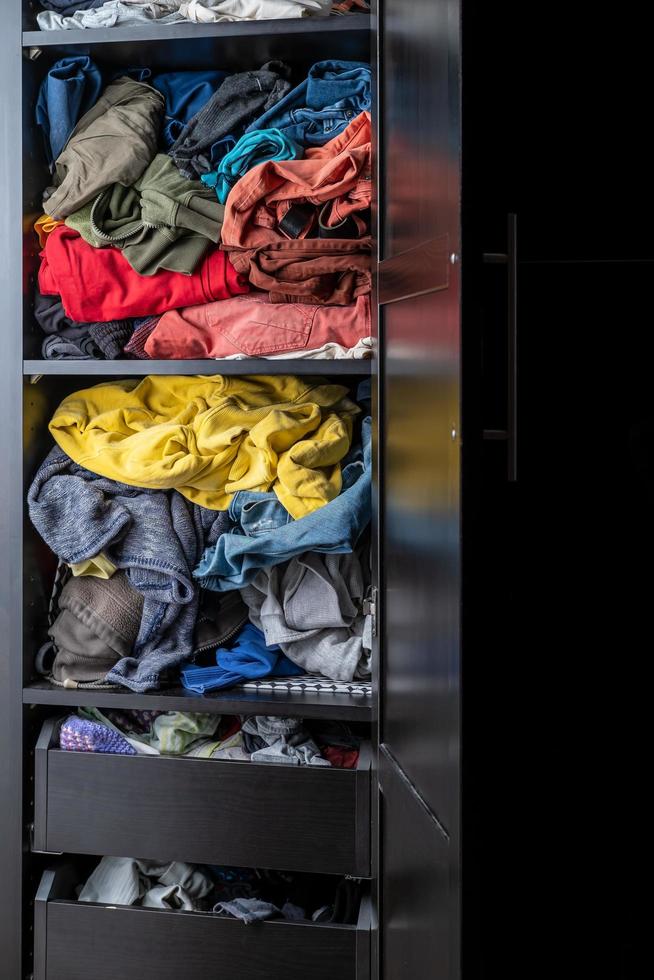 Variety of brightly colored clothes lie casually on a shelf in a closet. photo