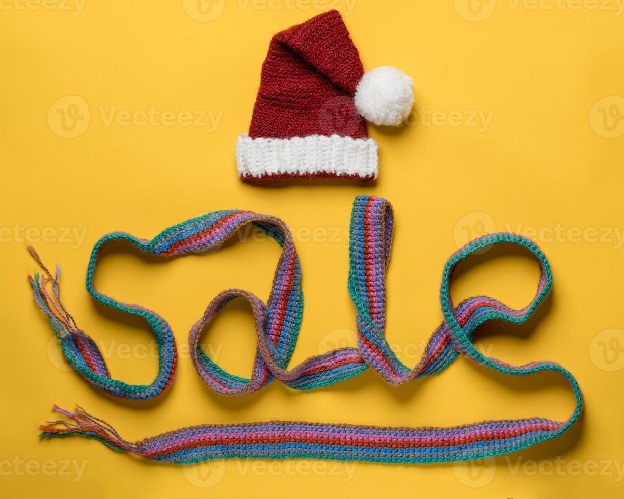 Inscription sale from a scarf and a hat of Santa Claus on top, on a yellow background. Concept of New Year's discounts and shopping. photo