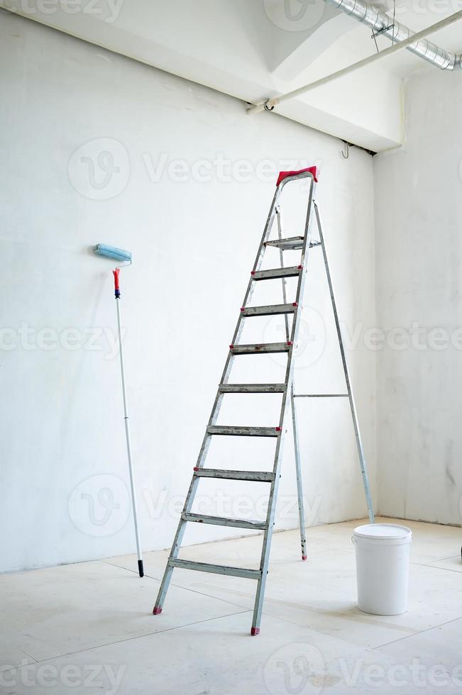 Stepladder, a closed plastic bucket of paint and a paint roller, in the room. Preparation for repair. photo