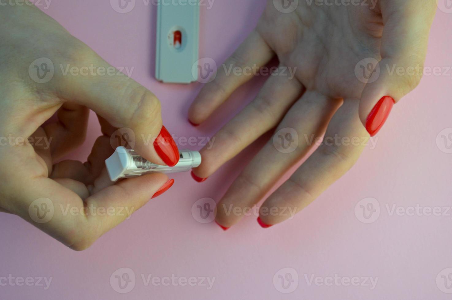 coronavirus test on a pink matte background. medical procedure. the girl pierces her finger with a lancet and adds a drop of blood to the sensitive test strip photo