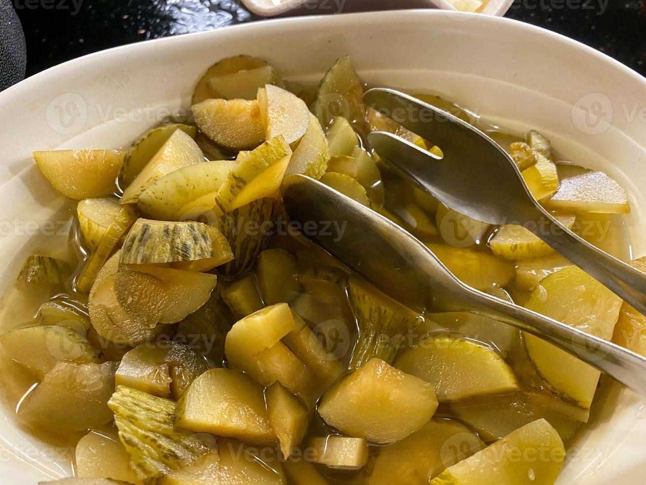 Delicious green fresh pickled cucumbers cut into small pieces, healthy vegetable salad sliced in a plate with tongs photo