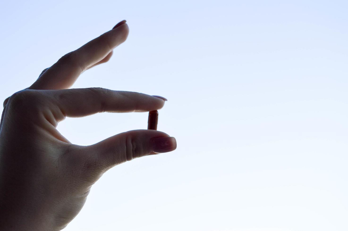 hermosa mano femenina sostiene una cápsula de píldora farmacéutica médica del coronavirus covid-19 para el tratamiento de enfermedades y virus en un fondo azul del cielo foto