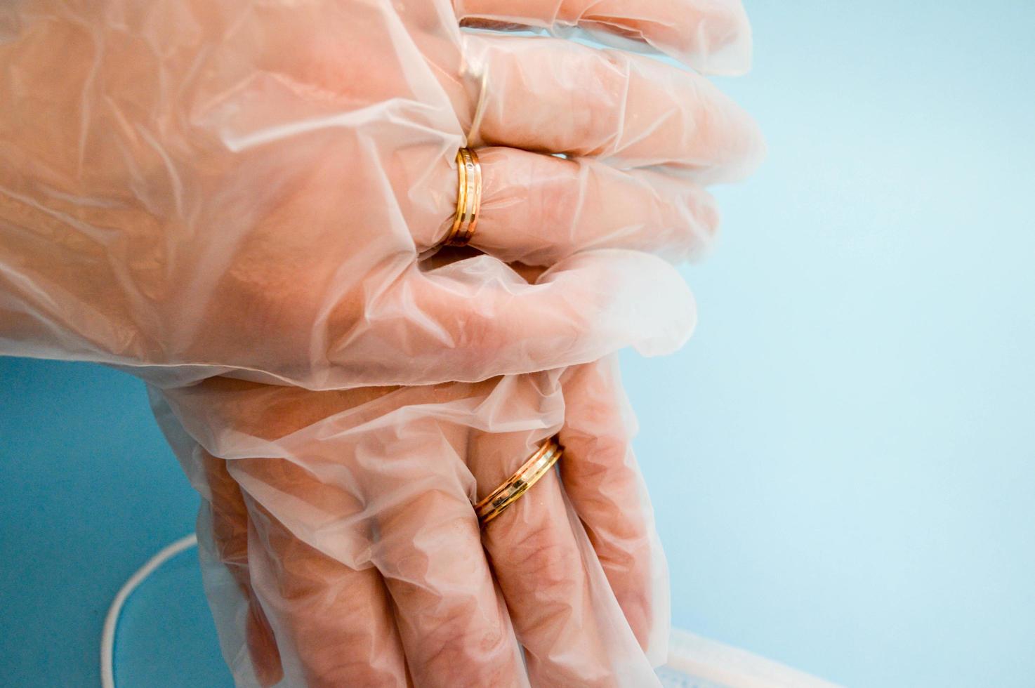 anillos de boda de oro en las manos con guantes desechables de caucho médico protector para la protección contra enfermedades mortales peligrosas de microbios y virus por coronavirus covid-19 sobre un fondo azul foto