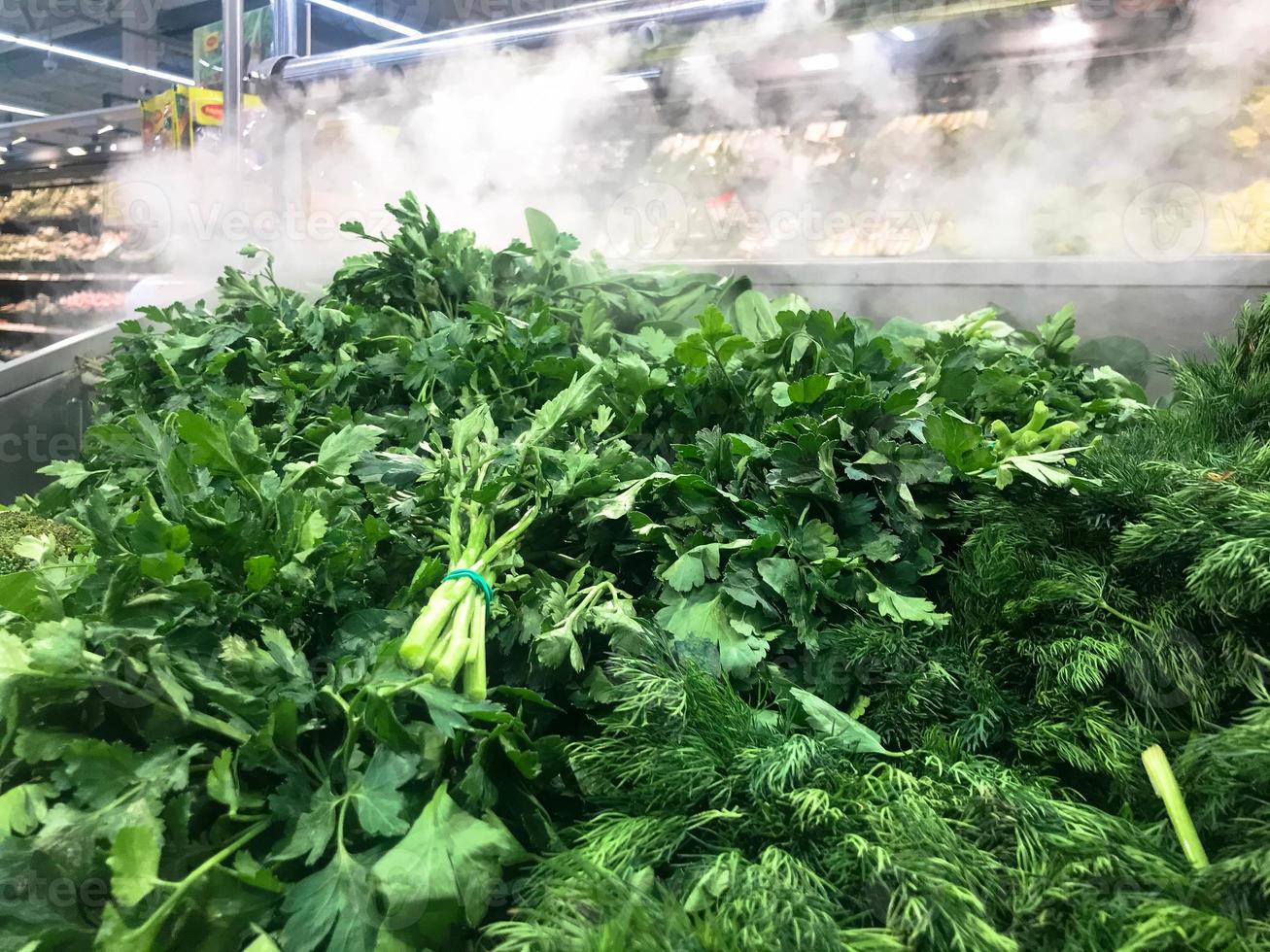 Green fresh environmentally friendly greens of parsley plants dill salad arugula onions and other plant foods lies in a modern refrigerator in a supermarket store on the counter. The background photo