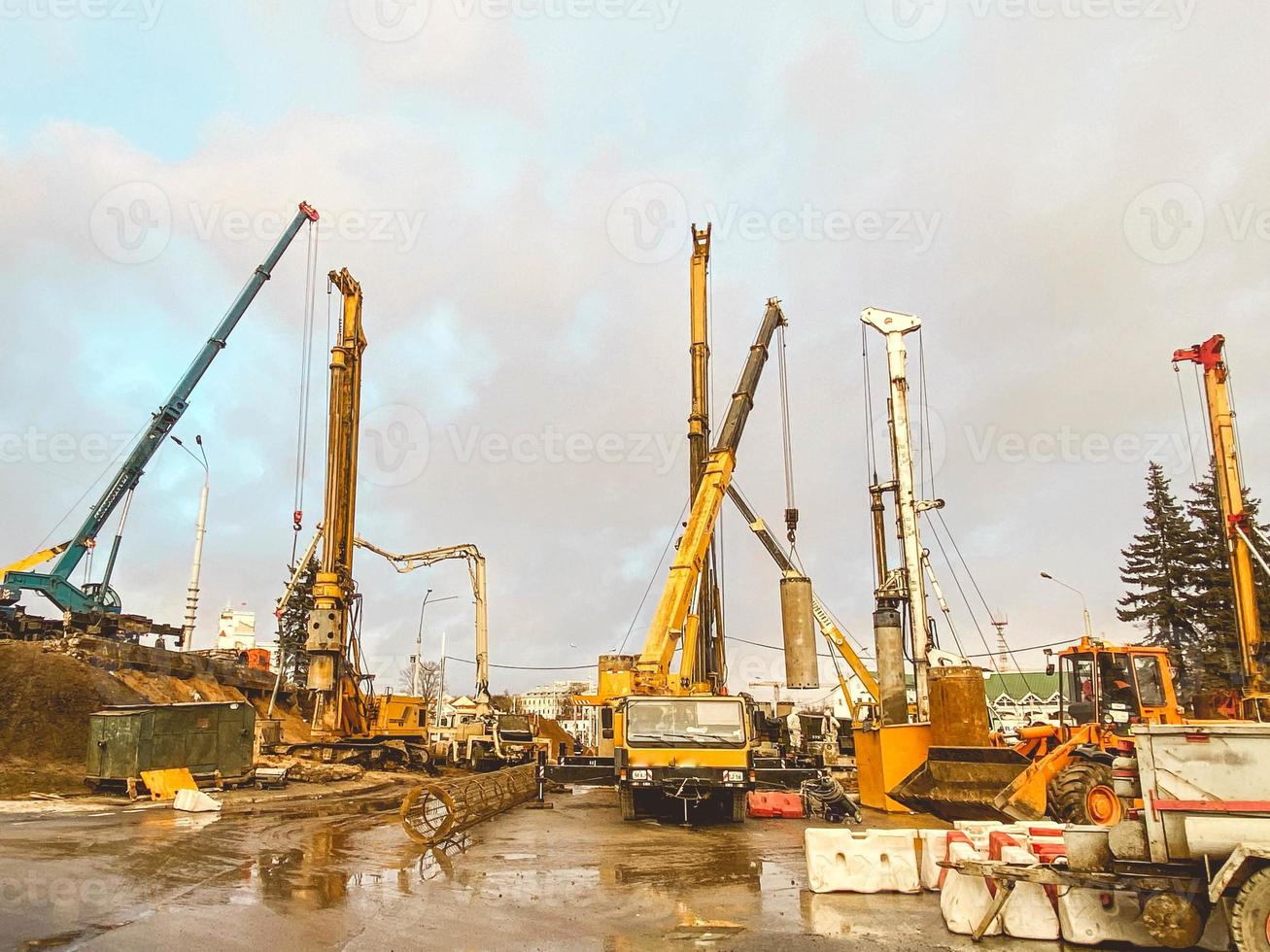 construction equipment at the overpass repair site. large concrete blocks are erected by cranes. next to a large truck. construction site on wet asphalt with puddles photo