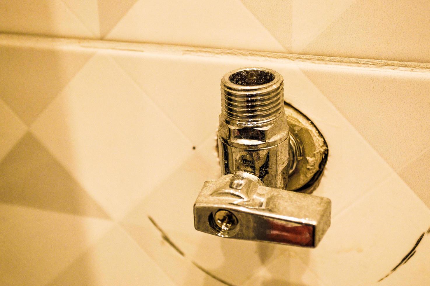 Metallic iron shiny chrome plumbing fittings with thread and valve in the wall of ceramic tiles photo