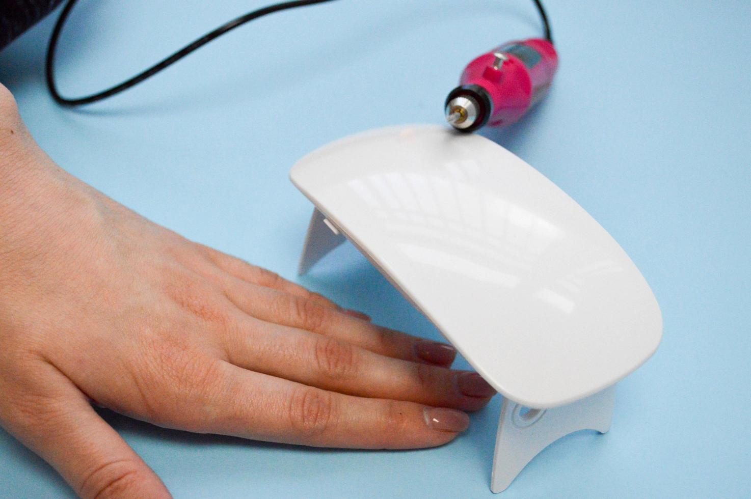 The process of making a beautiful manicure on the hands on the fingers with the help of a special machine and a lamp for drying the varnish in the nail beauty salon on a blue background photo