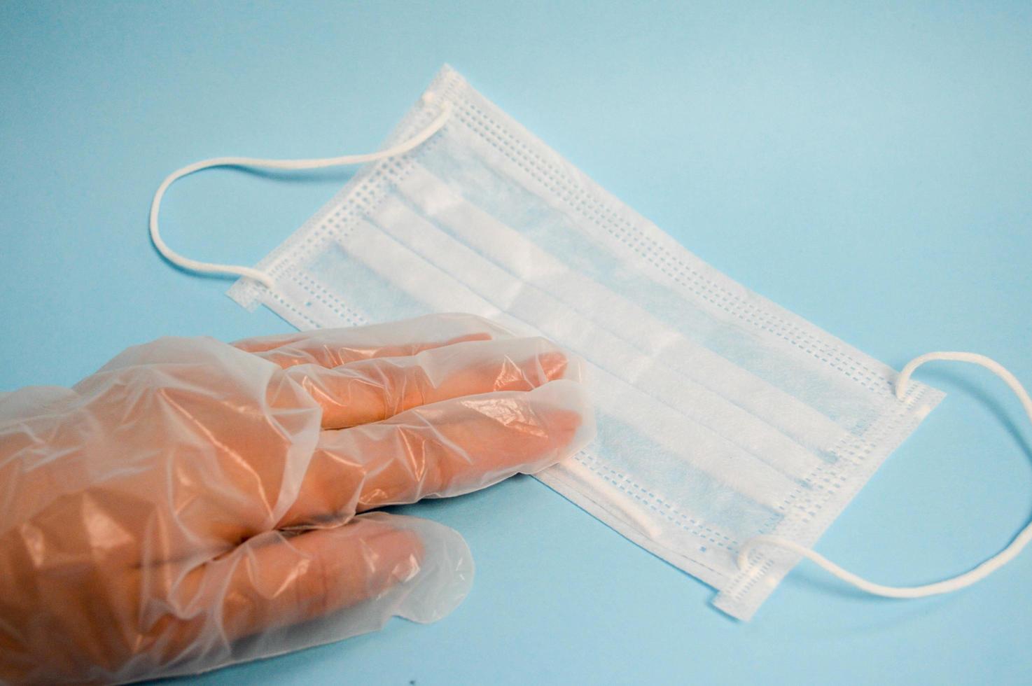 A hand in a plastic glove holds a disposable protective medical mask for protection against dangerous deadly diseases of microbes and viruses by the coronavirus covidum-19 on a blue background photo