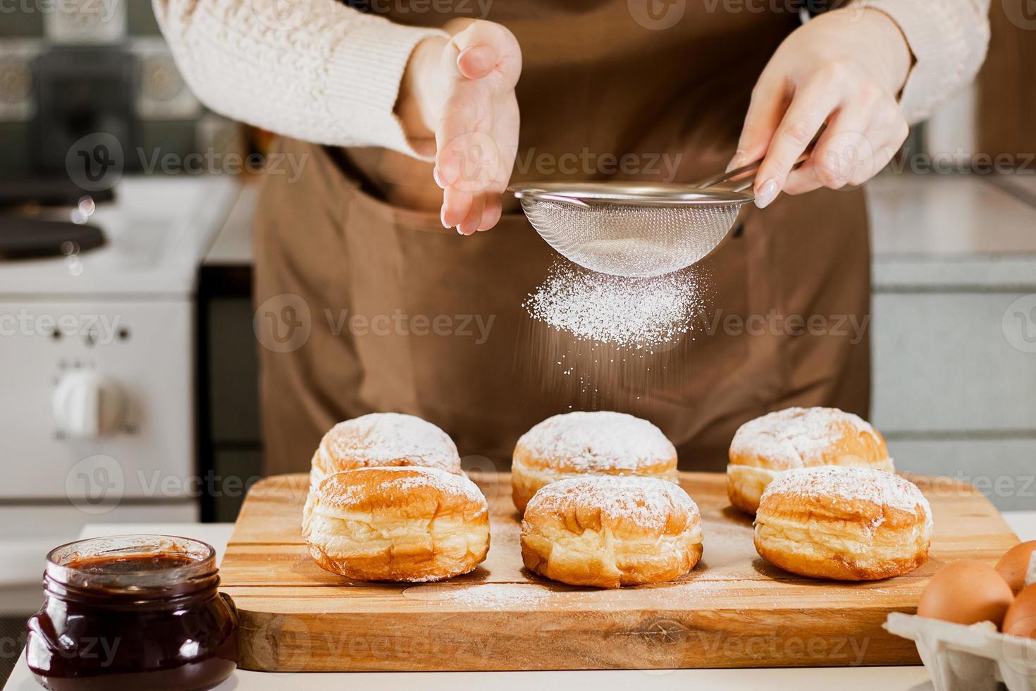 mujer prepara donas frescas con mermelada en la cocina de casa. cocina tradicional judía hanukkah sufganiyot. foto