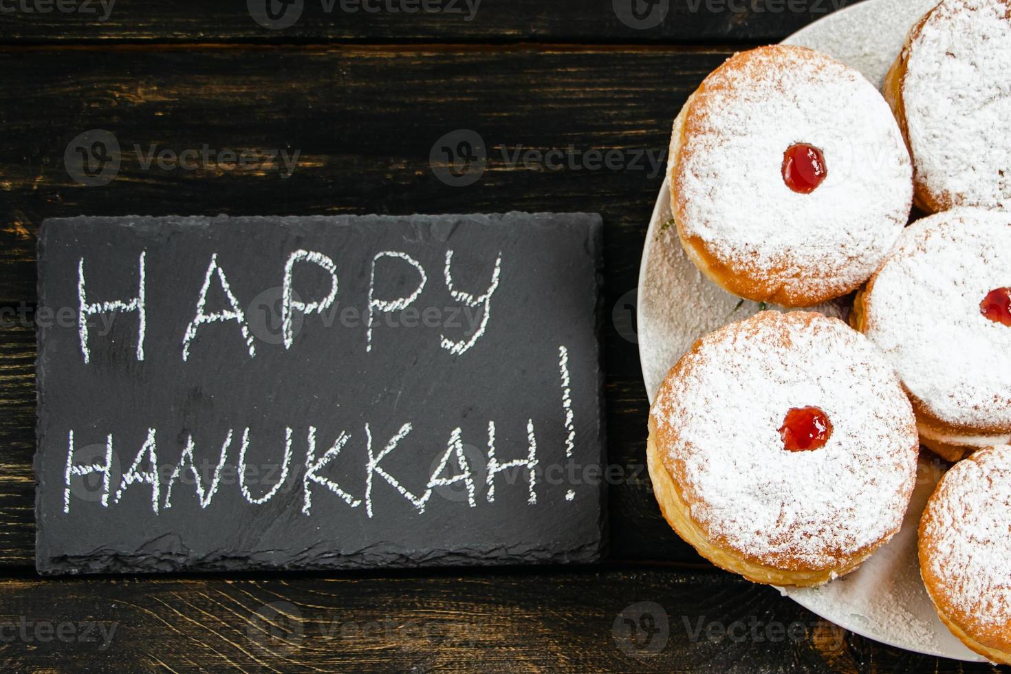 feliz Jánuca. postre tradicional sufganiyot sobre fondo de madera oscura. donuts, velas y regalos. celebrando la festividad judía. foto