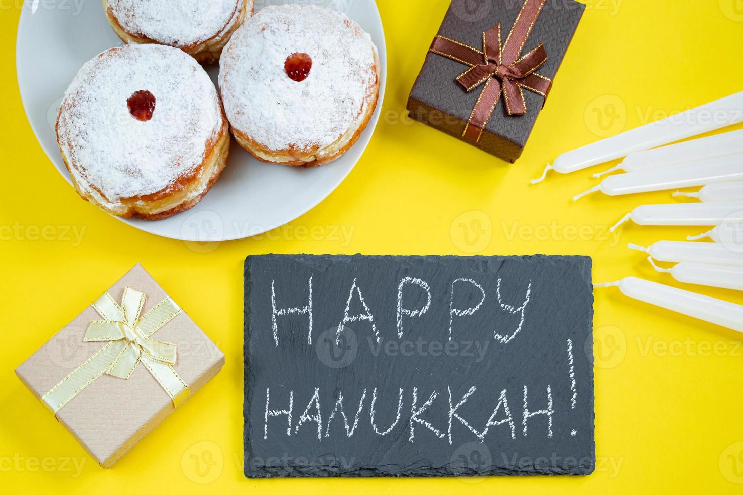 feliz Jánuca. postre judío sufganiyot sobre fondo amarillo. símbolos de la fiesta del judaísmo religioso. donuts, velas y regalo. foto