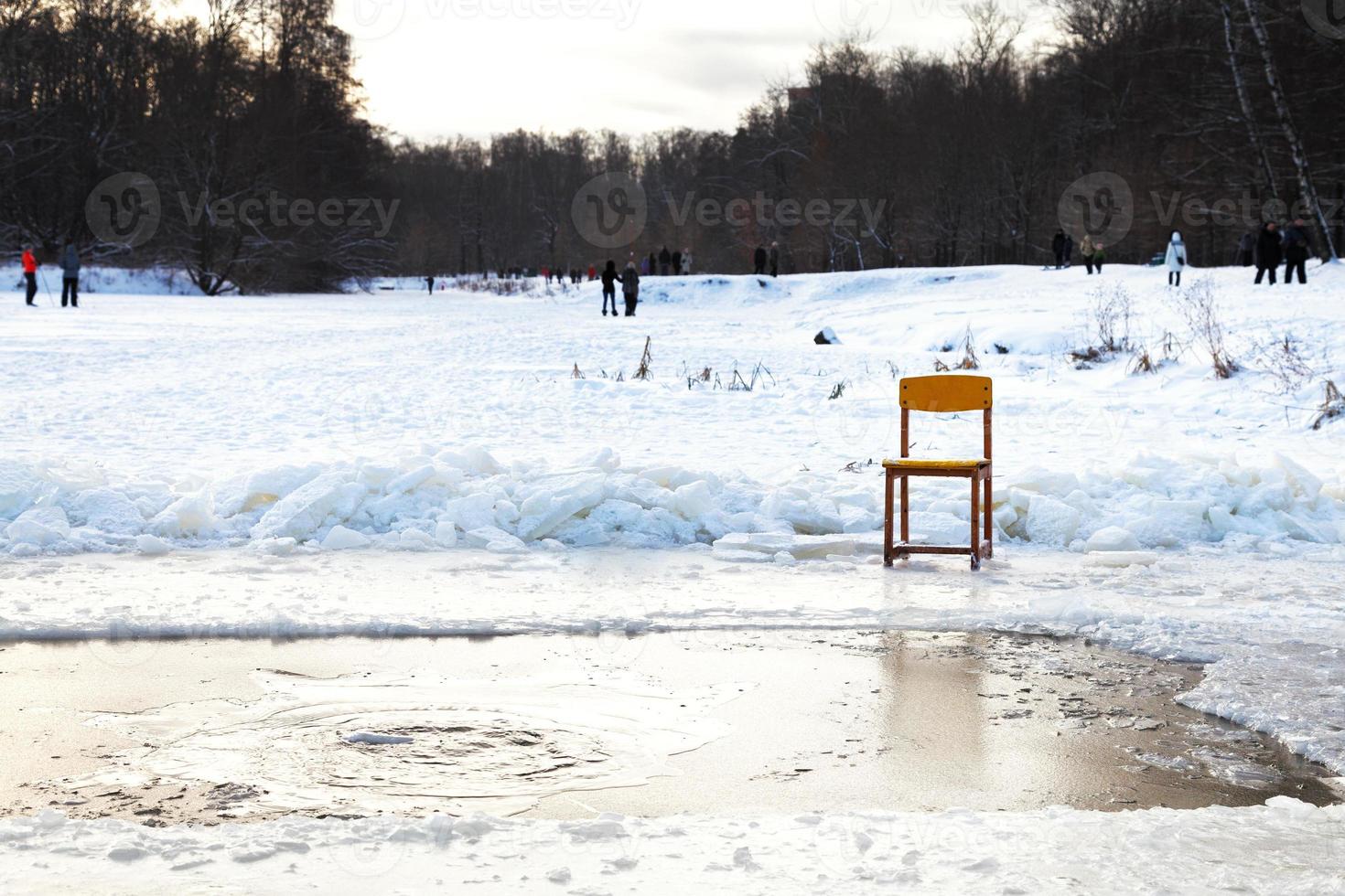 icebound chair near opening water in frozen lake photo