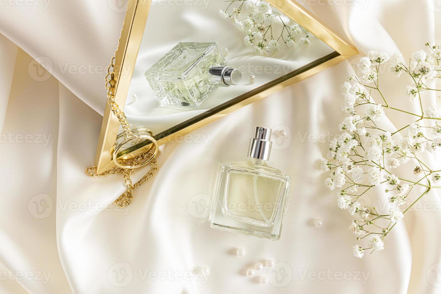 Frasco de perfume y elegante composición con flores de espejo y gipsófila sobre un fondo satinado pastel. una plantilla para perfume o agua de tocador. foto