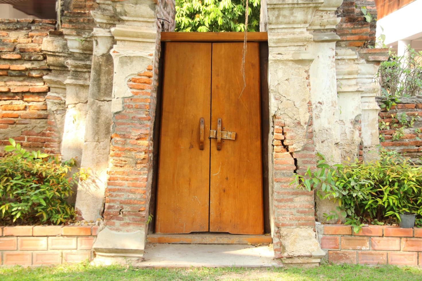 puerta de madera pintada de color marrón claro entre la pared de ladrillos rotos.la puerta está cerrada pero desbloqueada. foto