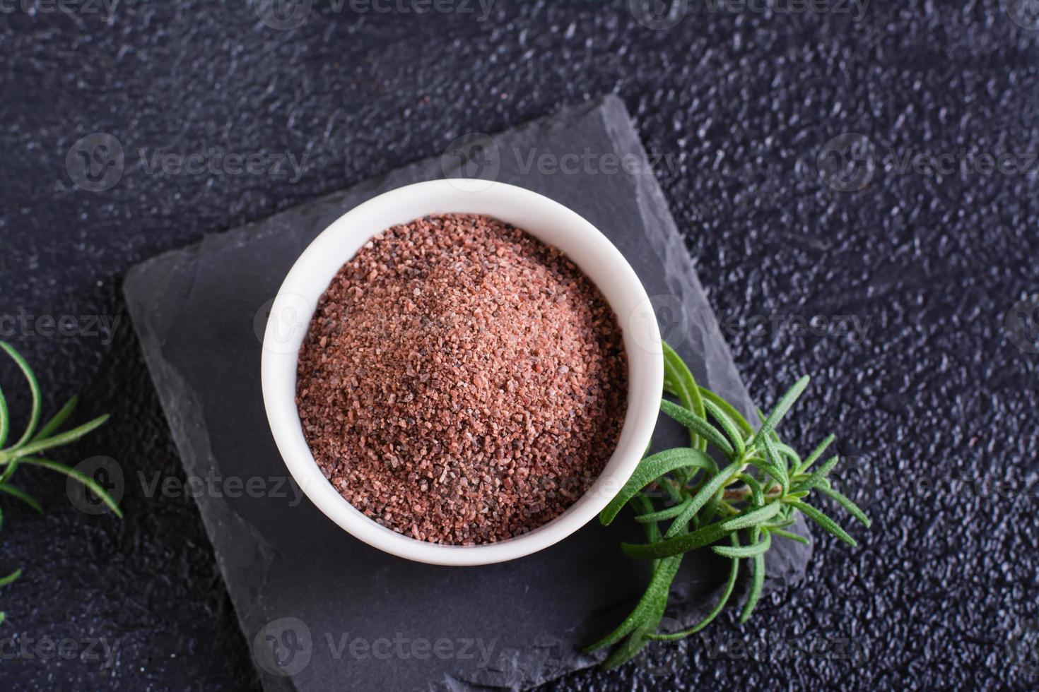 Black Himalayan rock salt in a bowl and rosemary on a black background. Top view. Closeup photo