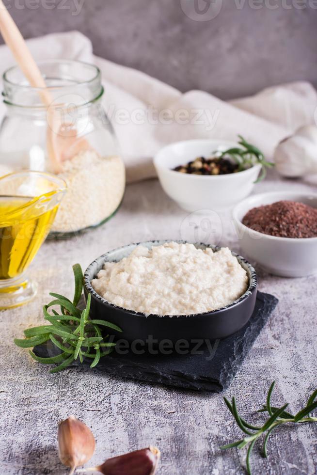 salsa tahini de semillas de sésamo en un bol e ingredientes para cocinar sobre la mesa. vista vertical foto